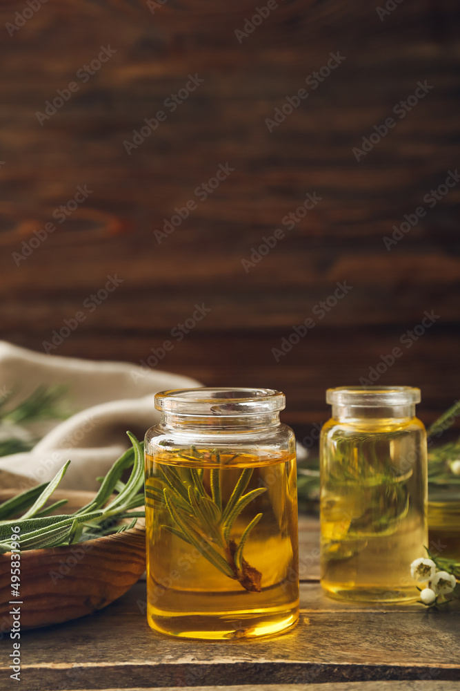 Bottles of natural rosemary essential oil on wooden background