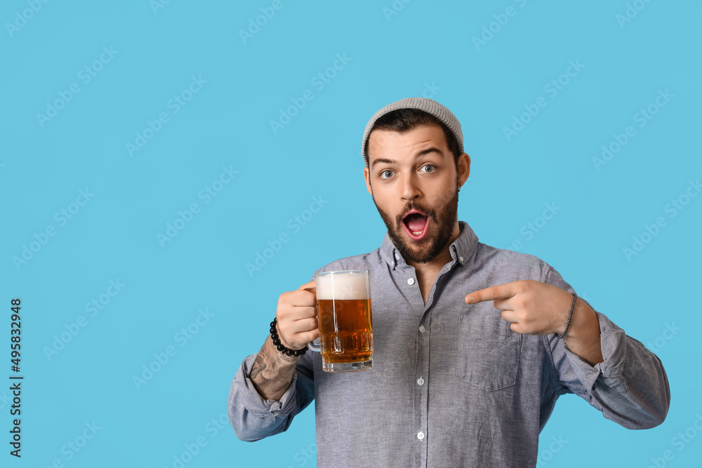 Surprised young bearded man pointing at glass of beer on blue background Surprised young bearded man pointing at glass of beer on blue background