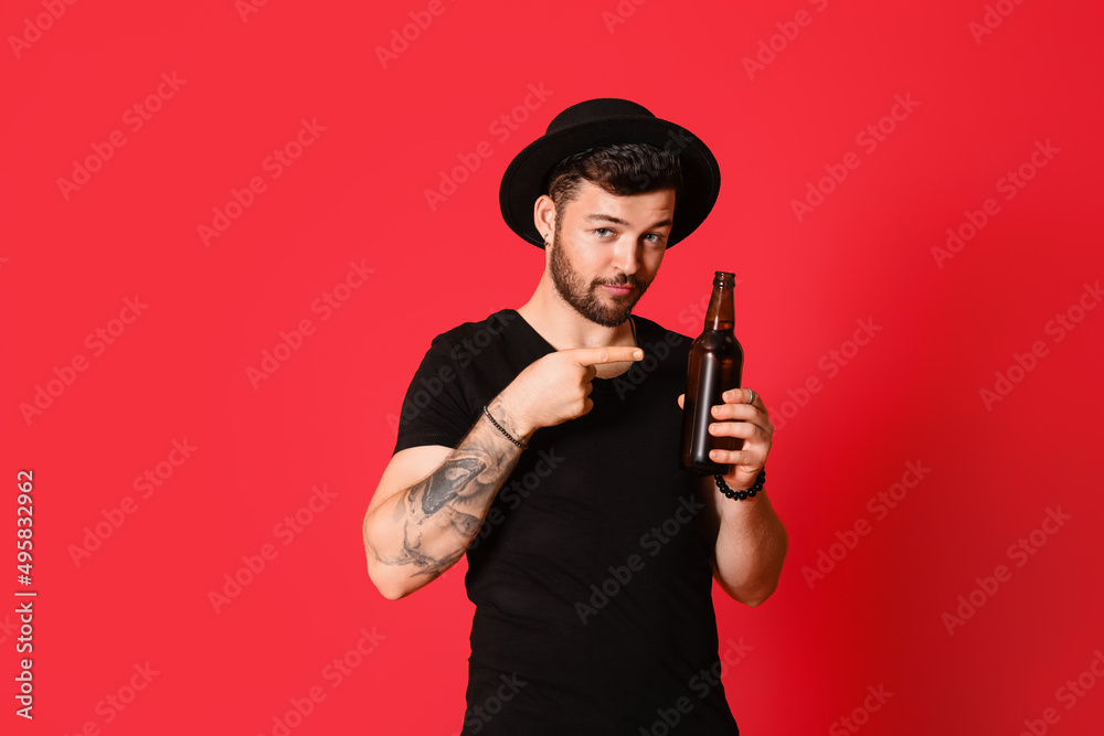 Stylish young man pointing at bottle of beer on red background Stylish young man pointing at bottle of beer on red background