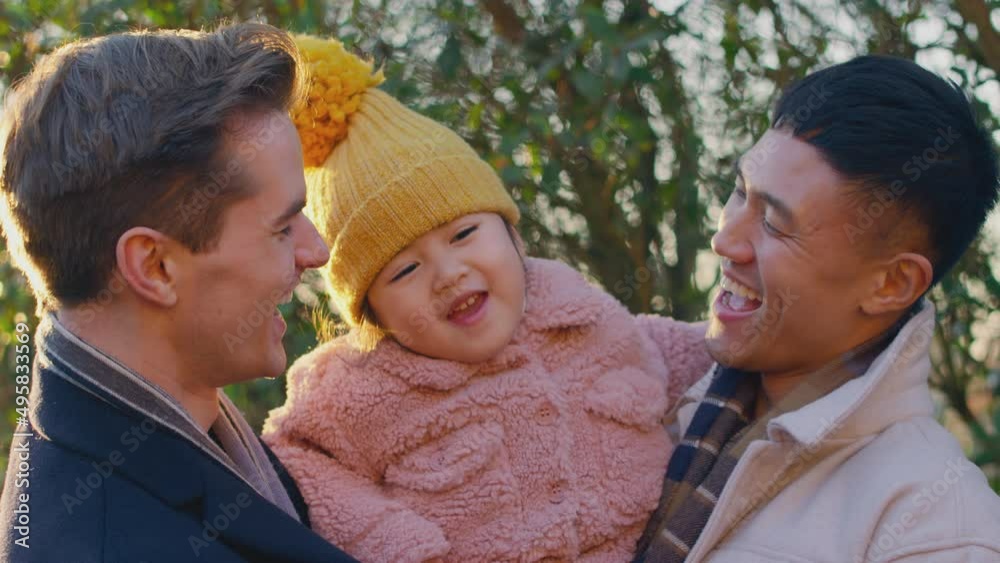 Portrait of family with two dads on walk in winter countryside carrying daughter between against flaring sun - shot in slow motion Portrait of family with two dads on walk in winter countryside carrying daughter between against flaring sun - shot in slow motion