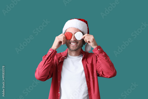 Young man in Santa hat with Christmas cookies on green background