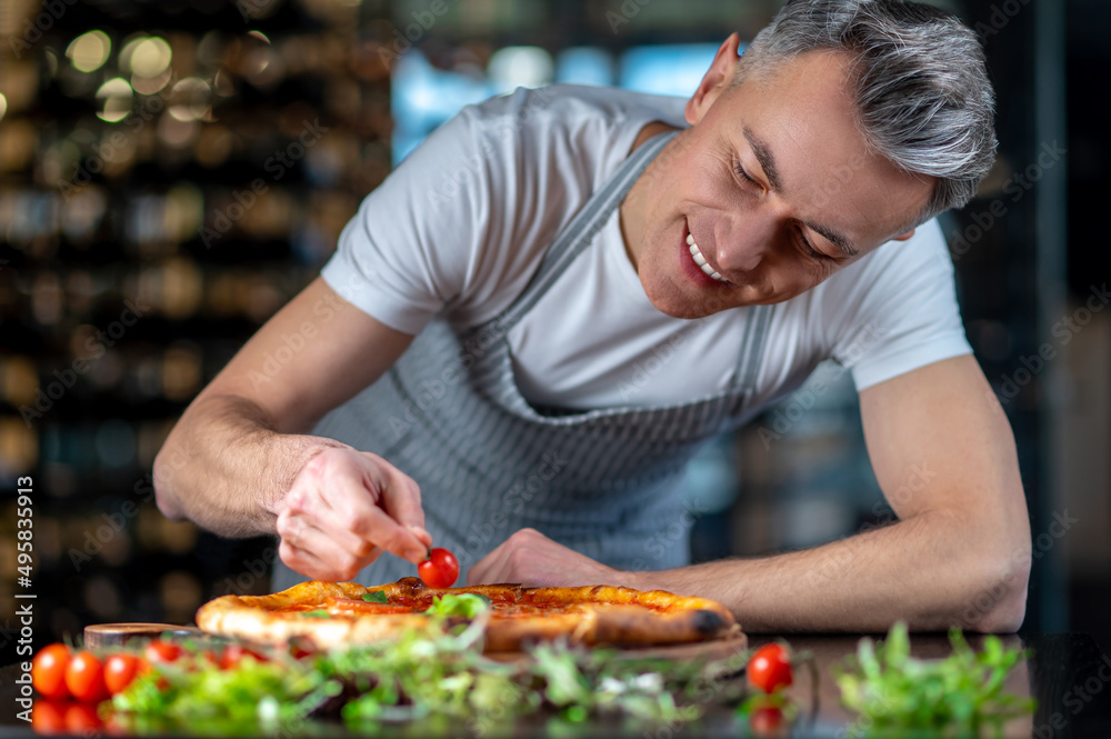 A chef making topping on a italian pizza