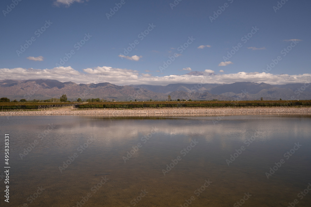 View of the artificial lake, vineyard and mountains in the horizon. Beautiful blue sky reflection in the water surface. 