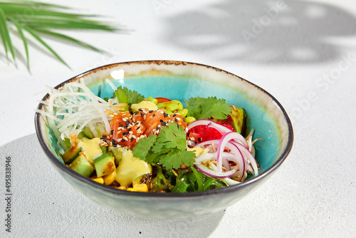 Hawaiian cuisine - Poke bowl with salmon, avocado, edamame and vegetables. Pokebowl in ceramic dish on white background with leaves. Summer menu in asian style. Healthy food.