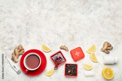 Cup of tea, pills for sore throat, lemon slices, ginger, jam and thermometer on light background
