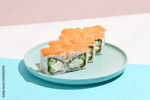Classic sushi roll with salmon outside, cheese and cucumber inside. Philadelphia maki in minimal style. Modern japanese menu concept. Salmon maki roll on ceramic plate on coloured background.
