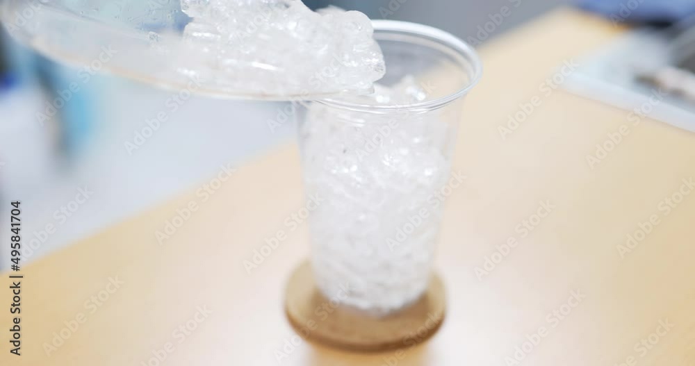 Pouring ice cube into a plastic glass.