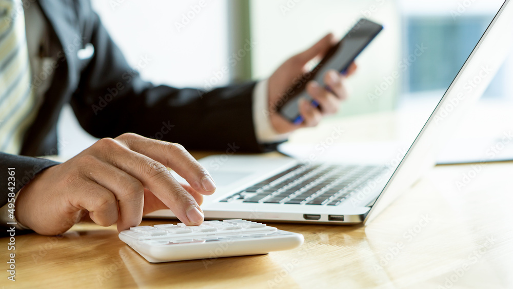 A businessman's hand presses a calculator and holds a smartphone and laptop in front of him. A businessman's hand presses a calculator and holds a smartphone and laptop in front of him.