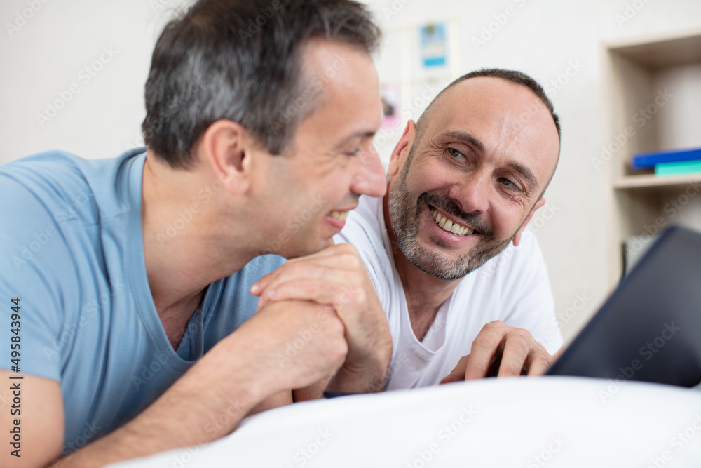 two men lying on the bed and using a laptop