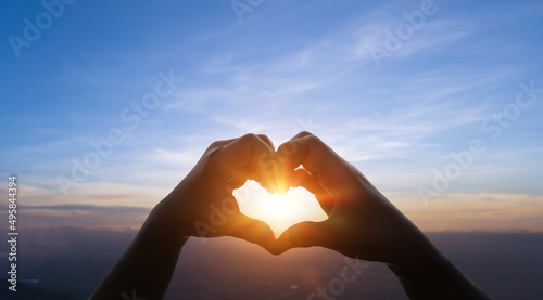 Child hands in heart shape against sky sunset background. Love concept.