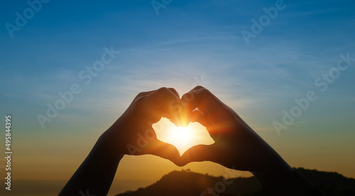 Child hands in heart shape against sky sunset background. Love concept.