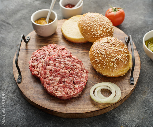The raw ingredients for the homemade burger on wooden board. Burger patties. Raw mince meat cutlet, ground beef and pork with bun. Grey background.