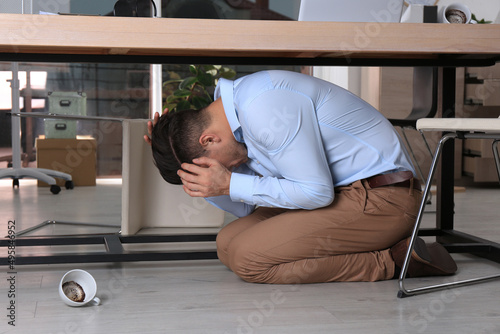 Fotografi Scared man hiding under office desk during earthquake