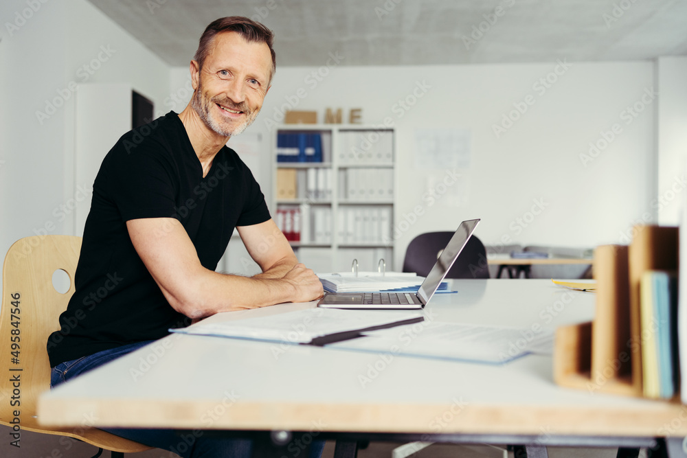 Fototapeta premium smiling man sitting in home office at desk, in front of laptop