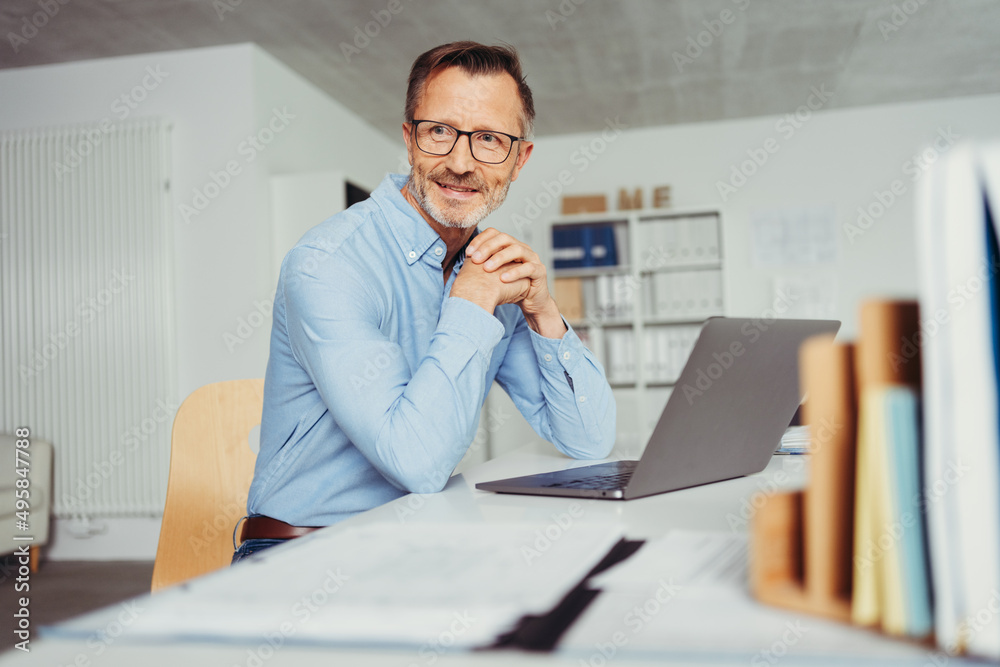 smiling man sitting in home office at desk, in front of laptop smiling man sitting in home office at desk, in front of laptop