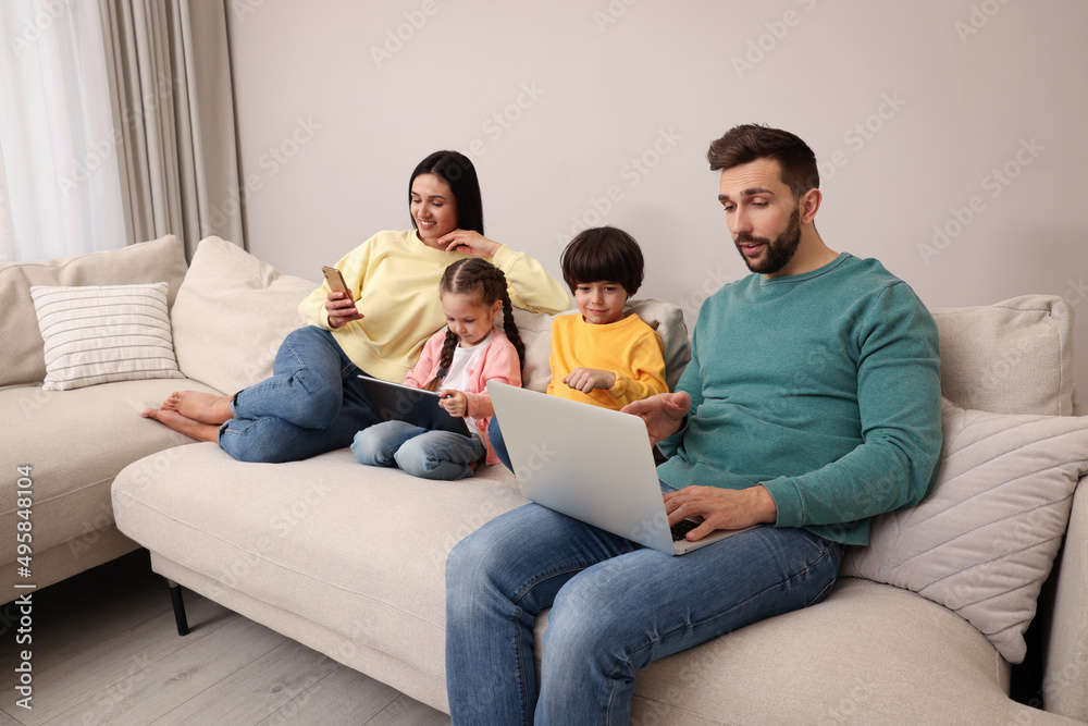 Happy family with gadgets on sofa in living room Happy family with gadgets on sofa in living room