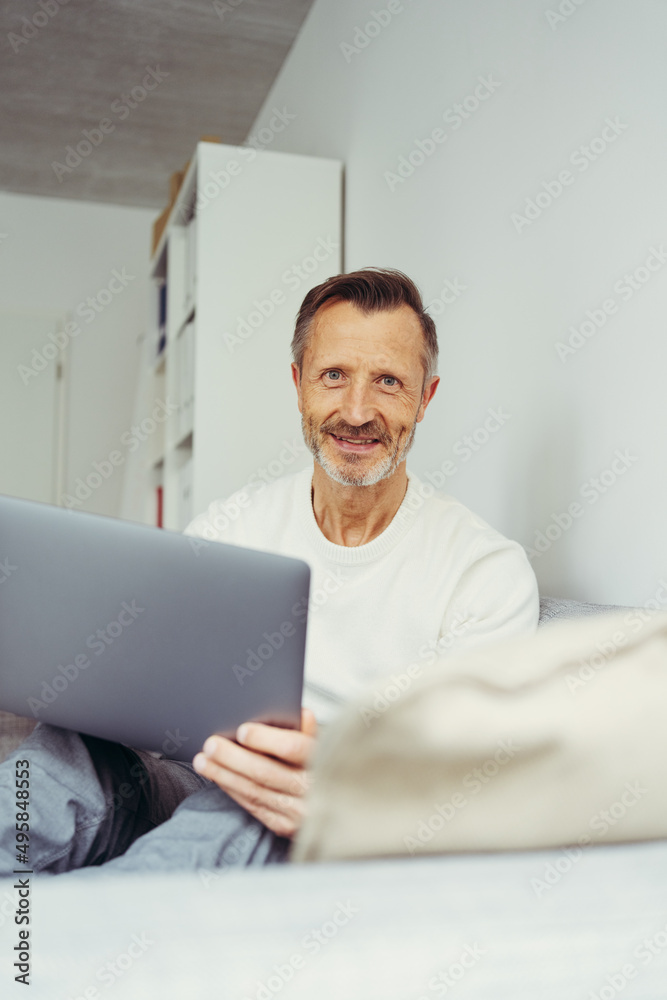 older man sits on sofa with laptop and looks into camera older man sits on sofa with laptop and looks into camera