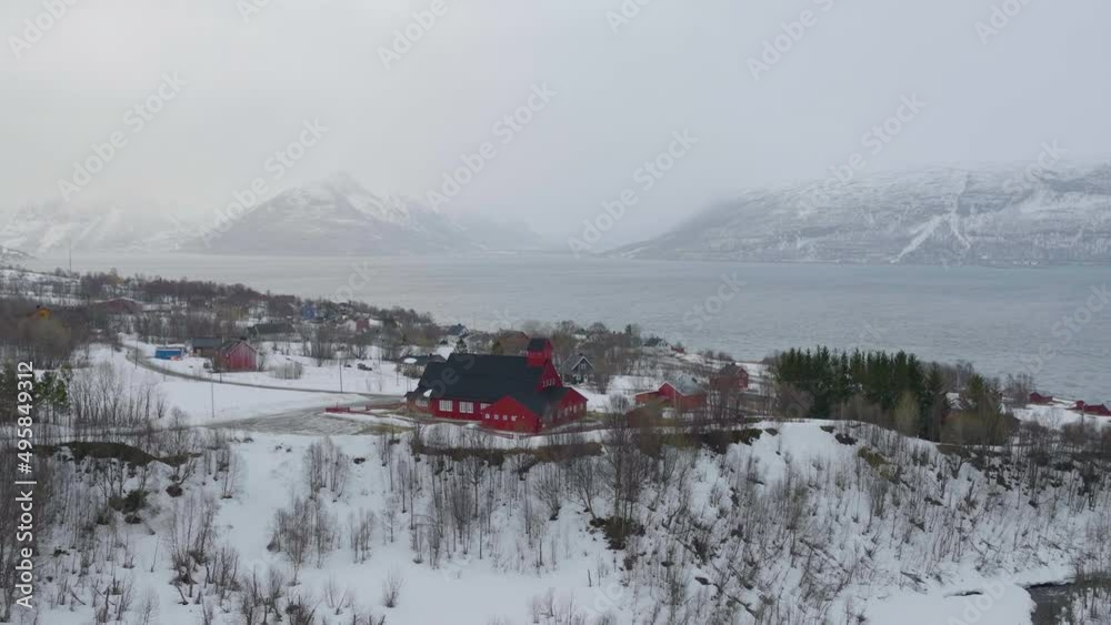 Aerial drone orbits around Kåfjord Church in Norway. Snow covered coastline, with mountainous background. Aerial drone orbits around Kåfjord Church in Norway. Snow covered coastline, with mountainous background.