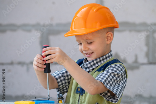 Little boy holding screwdriver. Kid twists bolt with screwdriver. Little Repairman with repair tool. Cute kid as a construction worker. Childrens play with a hammer pliers and screwdriver. Repair home