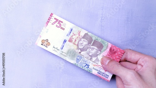 IDR Indonesian Rupiah the official currency of Indonesia. Man's hand is making a payment. Business Loan Income Money Investment Economy and Finance Concept Uang 75000 75.000 Rupiah. Prosperity Concept