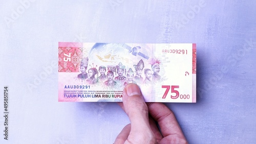 IDR Indonesian Rupiah the official currency of Indonesia. Man's hand is making a payment. Business Loan Income Money Investment Economy and Finance Concept Uang 75000 75.000 Rupiah. Prosperity Concept