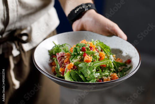 chef in a black suit holds in his hands bowl with salad on Dark grey black background 