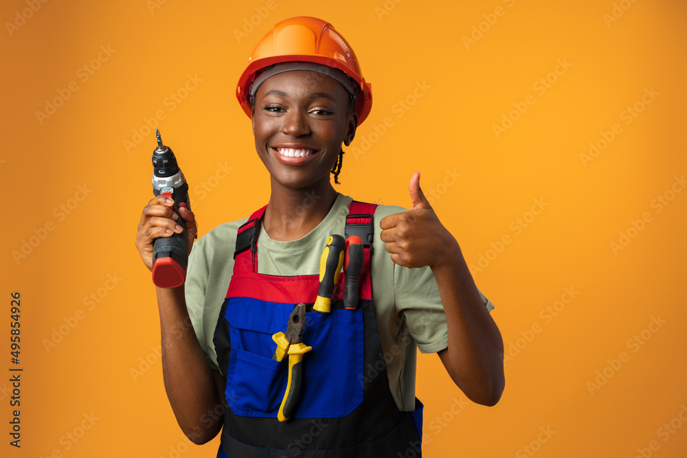 Smiling young african american woman in hardhat holding screwdriver tool in studio