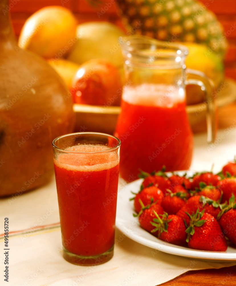Fresh strawberry juice glass and jar on tropical fruits background. Fresh strawberry juice glass and jar on tropical fruits background.