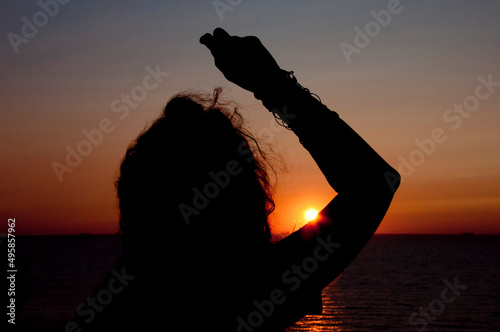 silhouette of young woman look at summer sunset sun and sky with seascape