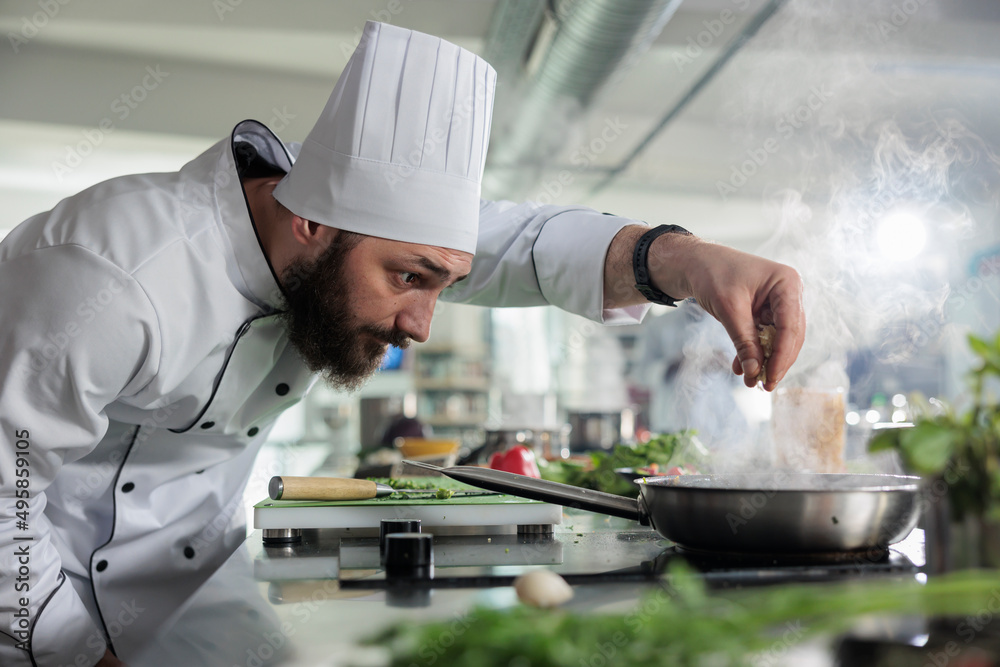 Food industry worker preparing ingredients for evening meal in professional kitchen. Head chef seasoning gourmet dish in pan while cooking fine dining food served at dinner service in restaurant. Food industry worker preparing ingredients for evening meal in professional kitchen. Head chef seasoning gourmet dish in pan while cooking fine dining food served at dinner service in restaurant.