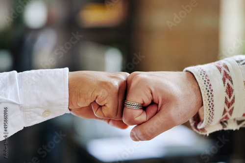 Close-up of hands of two young contemporary businessmen greeting each other by punch bump in front of camera in office