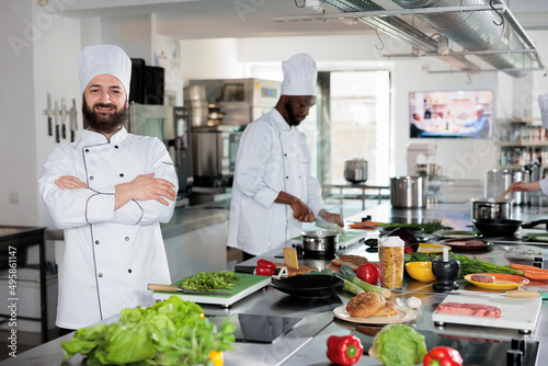Food industry worker with gourmet cuisine skills, preparing vegetables and spices for delicious meal. Sous chef wearing cooking uniform, standing in restaurant professional kitchen looking at camera.