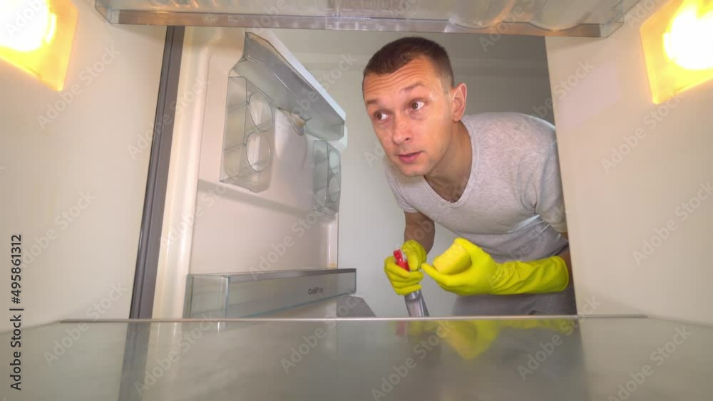 young white European opens refrigerator to wash it. Wearing gloves, with a sponge and spray from sniffing and plugging the nose with your hand because of the terrible smell. Germs and freon leakage. young white European opens refrigerator to wash it. Wearing gloves, with a sponge and spray from sniffing and plugging the nose with your hand because of the terrible smell. Germs and freon leakage.