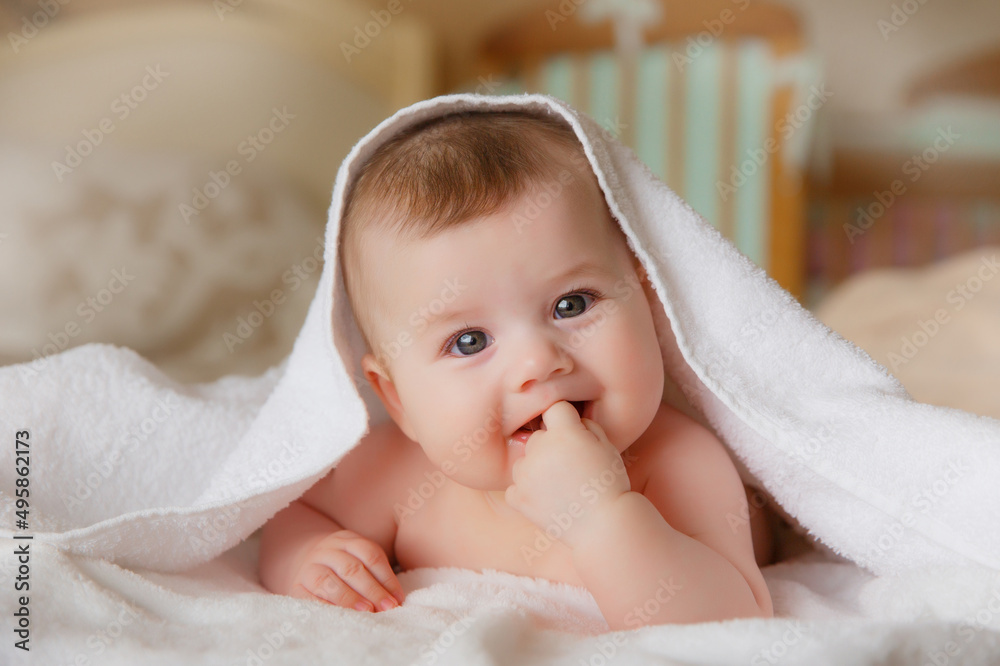 charming baby girl in a white towel or blanket in a white bedroom. A newborn baby is resting in bed. Portrait of a Caucasian child. The concept of kindergarten and infancy. charming baby girl in a white towel or blanket in a white bedroom. A newborn baby is resting in bed. Portrait of a Caucasian child. The concept of kindergarten and infancy.