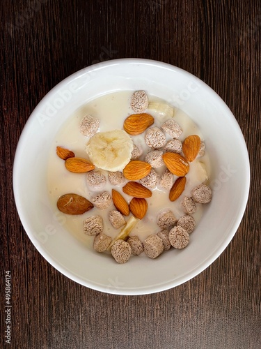 large vertical photo. homemade food. white yogurt with bran and slices of banana with almonds in a round ceramic plate with a pattern. useful vitamin breakfast. eco. bio. diet food.