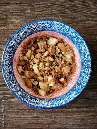 large vertical photo. homemade food. spelled groats boiled with banana slices and almonds in a round ceramic plate with a pattern. useful vitamin breakfast. eco. bio. diet food