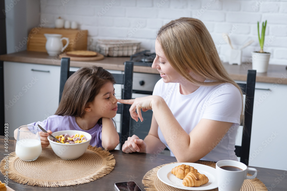 young blond women is having breakfast with her little daughter at kitchen
