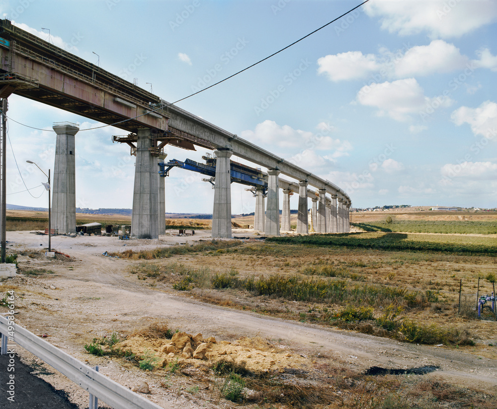 Bridge under construction, pillars and elevated road across an arid landscape.