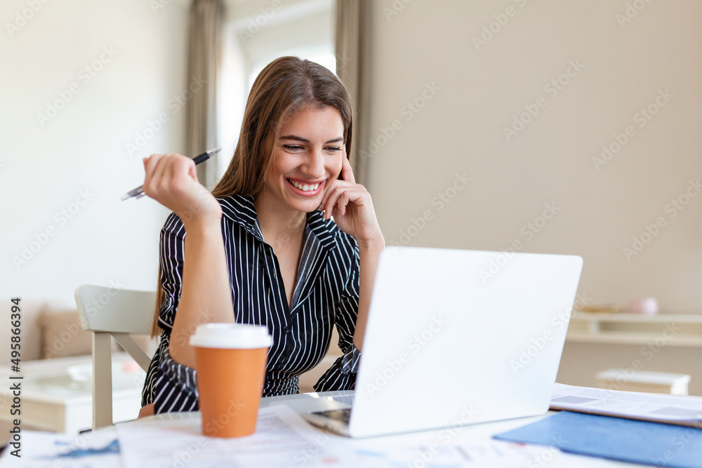 Business Women at home during pandemic isolation working on laptop and drinking coffee.Image of young pleased happy cheerful cute beautiful business woman sit indoors in office using laptop computer Business Women at home during pandemic isolation working on laptop and drinking coffee.Image of young pleased happy cheerful cute beautiful business woman sit indoors in office using laptop computer
