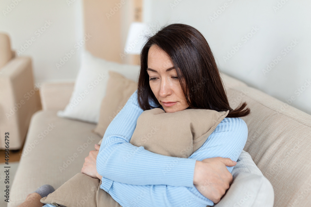 Frustrated Asian lady sitting on sofa, cuddling pillow, looking away at window. Lost in thoughts unhappy stressed woman regretting of wrong decision, spending time alone in living room. Frustrated Asian lady sitting on sofa, cuddling pillow, looking away at window. Lost in thoughts unhappy stressed woman regretting of wrong decision, spending time alone in living room.