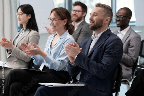 Quadro em tela Two rows of happy young intercultural employees clapping hands to speaker after