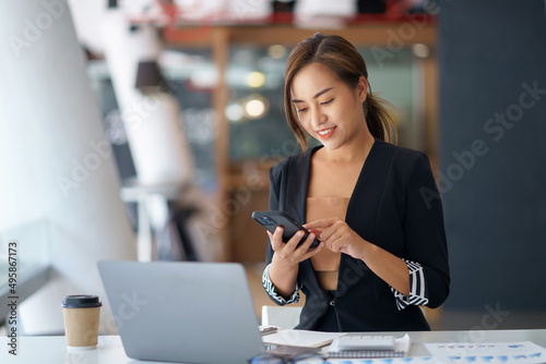 Charming young Asian businesswoman with a smile sitting holding smartphone at the office.