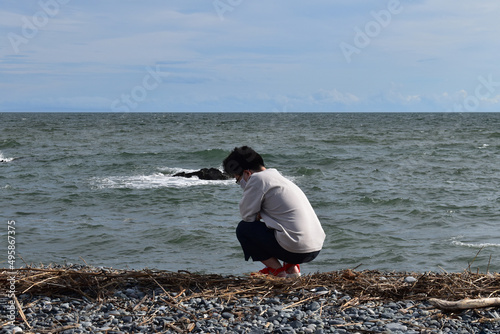 Obraz na plátně A man squatting and waiting for driftwood on the shore full of twigs on the beac