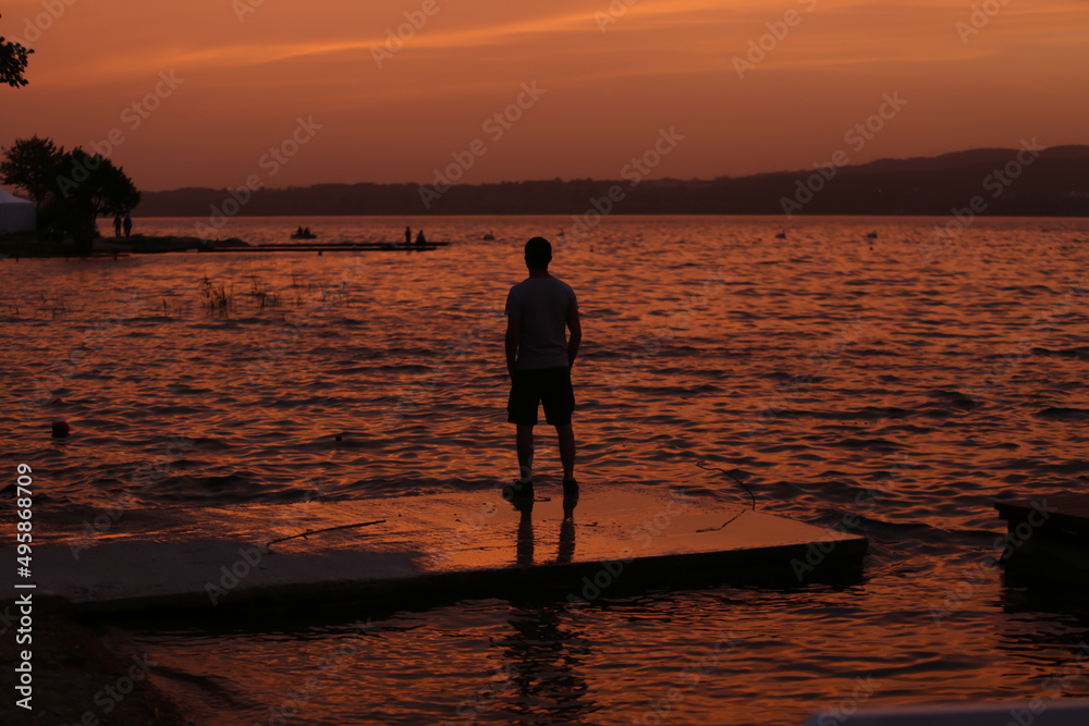 Man looking towards horizon by lake at sunset