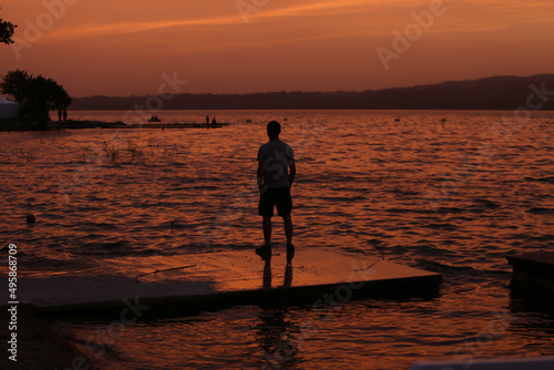 Man looking towards horizon by lake at sunset