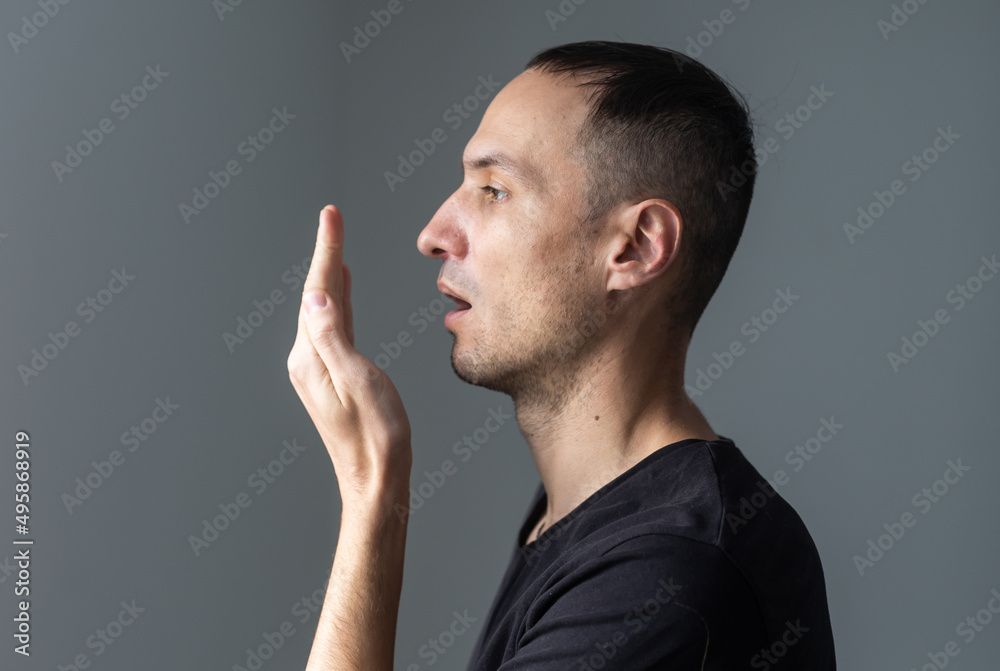 Close up of a good-looking man putting his hand in front of his mouth and checking his bad breath Close up of a good-looking man putting his hand in front of his mouth and checking his bad breath