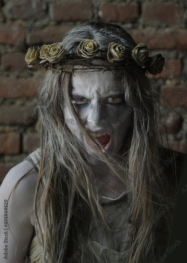 A teenage girl dressed as a Halloween horror figure. 
Her face is filled with horror as she screams at the 
camera. She wears a thorny floral crown on her head