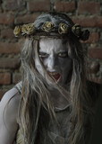 A teenage girl dressed as a Halloween horror figure. 
Her face is filled with horror as she screams at the 
camera. She wears a thorny floral crown on her head