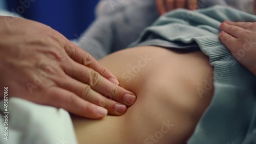 Doctor hands touching stomach closeup. Sick little girl lying in hospital bed.