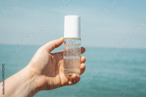 Girl's hand holding cosmetic transparent bottle outside in front of sea coast. Idea for fresh marine scented cosmetics mock up. 